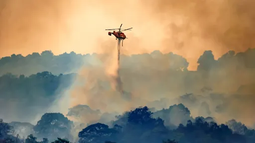 This is an image of an emergency helicopter flying over a forest fire in the mountains