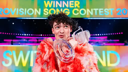 This is a close up photo shot of Nemo from Switzerland holding the Eurovision Song Contest trophy after winning the Grand Final
