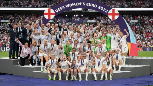 This is a photo of the England women's football team on the winner's podium cheering with the trophy after winning against Germany in the UEFA Women's EURO 2022 Final