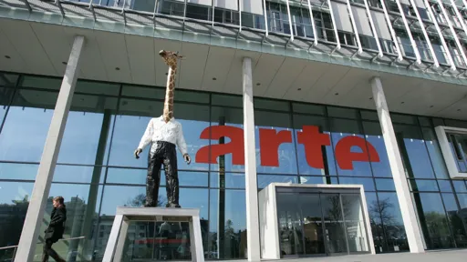 This is a photo of the ARTE building in France - it has the red ARTE lettering on the outside of the glass building and a colourful sculpture of a giraffe at the front door.